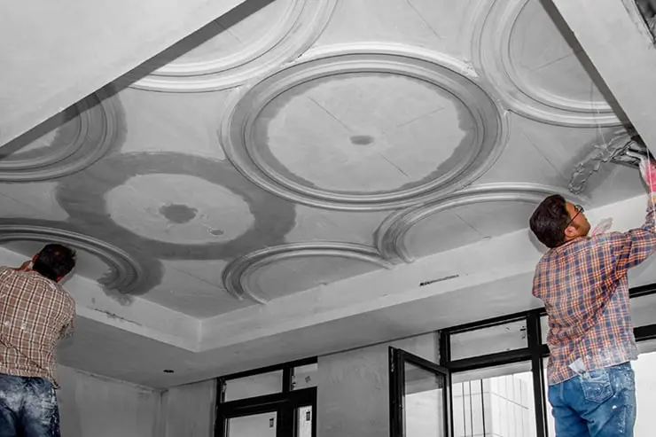 Two workers installing a decorative gypsum false ceiling with circular cornice patterns in a Dubai property, a ceiling service by MWADB Technical Services